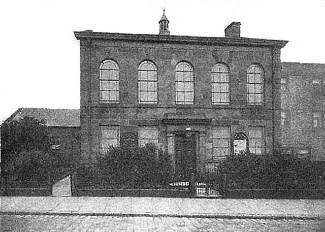 A black and white picture of the old Moorhouse Methodist Chapel, a building with large windows and a decorative top, surrounded by greenery.